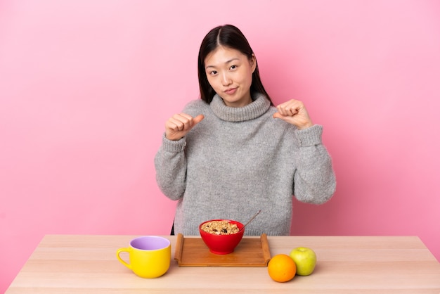 Giovane ragazza cinese facendo colazione in un tavolo orgoglioso e soddisfatto di sé