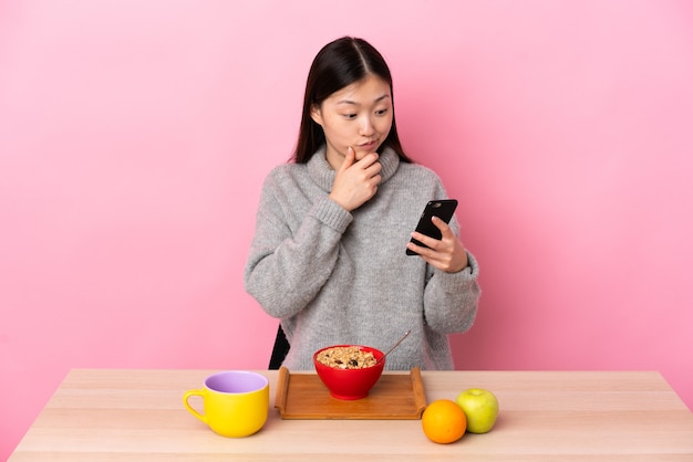 Young Chinese girl  having breakfast in a table thinking and sending a message