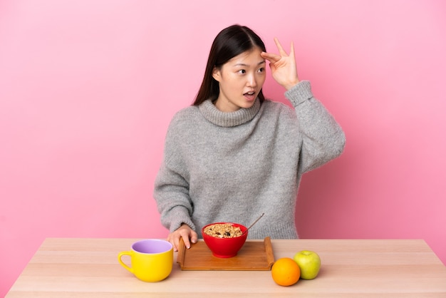 Young Chinese girl  having breakfast in a table with surprise expression while looking side