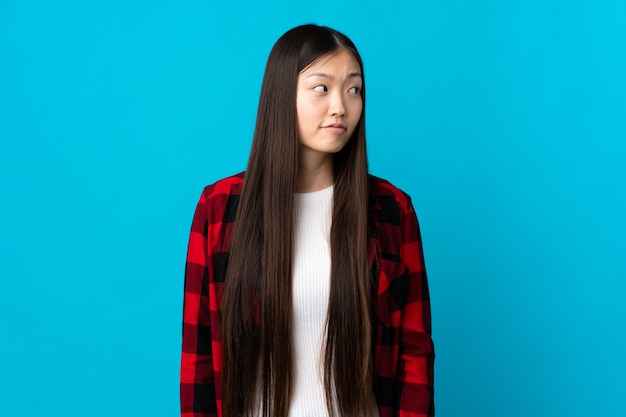 Young Chinese girl over isolated blue background making doubts gesture looking side