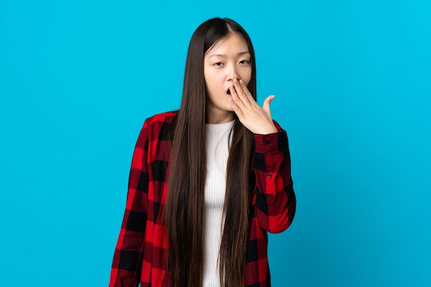 Young Chinese girl over isolated blue background yawning and covering wide open mouth with hand