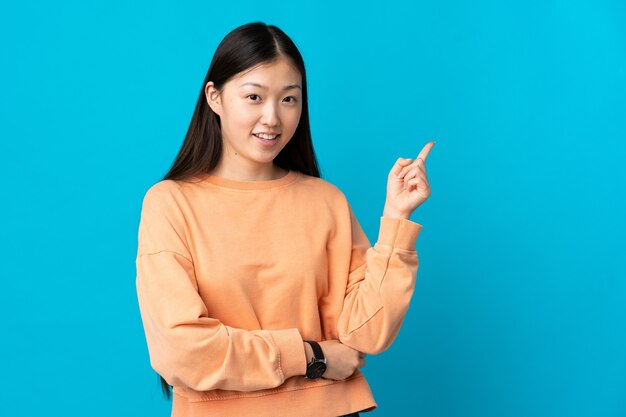 Young Chinese girl on isolated blue happy and pointing up