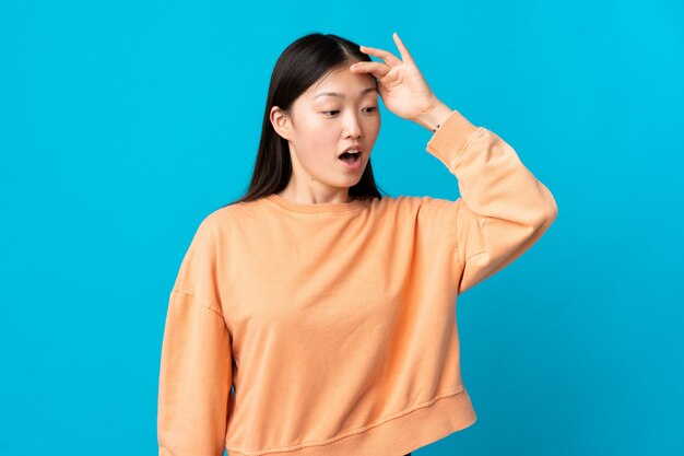 Young Chinese girl over isolated blue wall doing surprise gesture while looking to the side