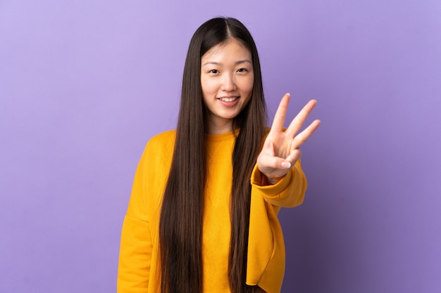 Young Chinese girl over isolated purple wall happy and counting three with fingers