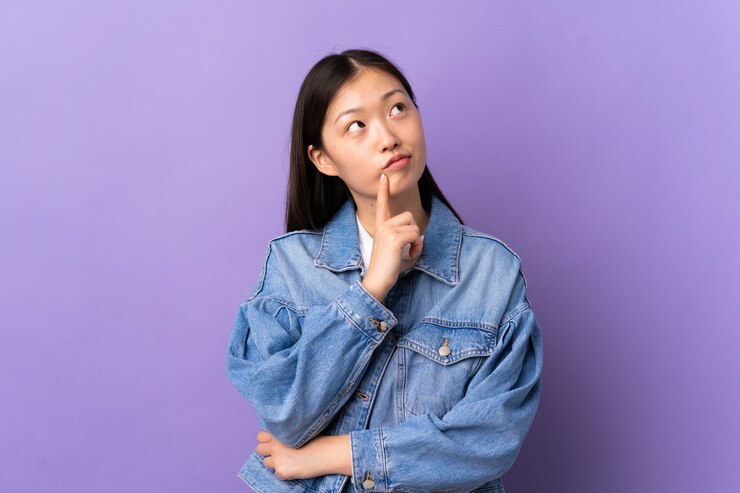 Photo 見上げている間疑いを持っている孤立した紫色の壁の上の若い中国の女の子