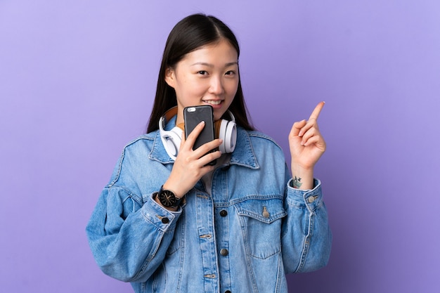 Giovane ragazza cinese sopra musica d'ascolto della parete viola isolata con un mobile e cantando