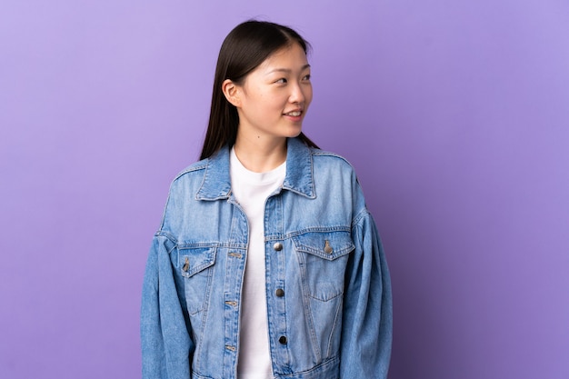 Young Chinese girl over isolated purple wall looking to the side and smiling