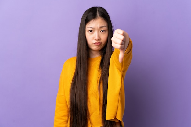 Young Chinese girl over isolated purple wall showing thumb down with negative expression