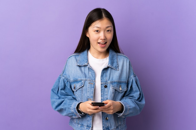 Young Chinese girl over isolated purple wall surprised and sending a message