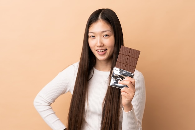 Young Chinese girl over isolated taking a chocolate tablet and happy