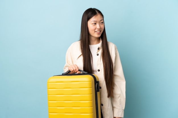 Young Chinese girl over isolated wall in vacation with travel suitcase