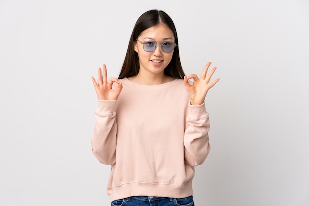 Young Chinese girl over isolated white showing ok sign with two hands