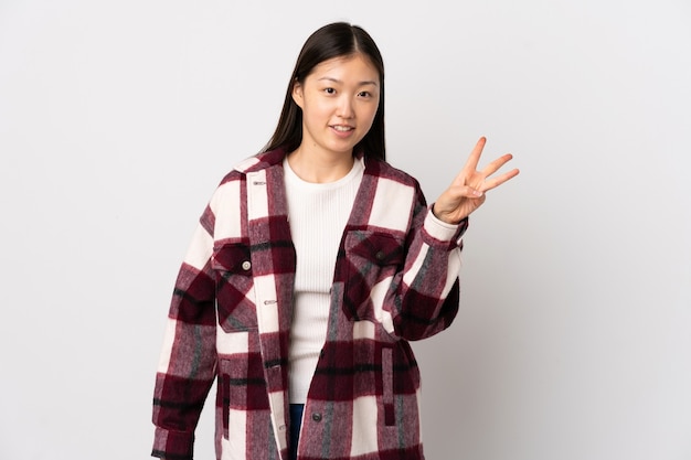 Young Chinese girl over isolated white wall happy and counting three with fingers