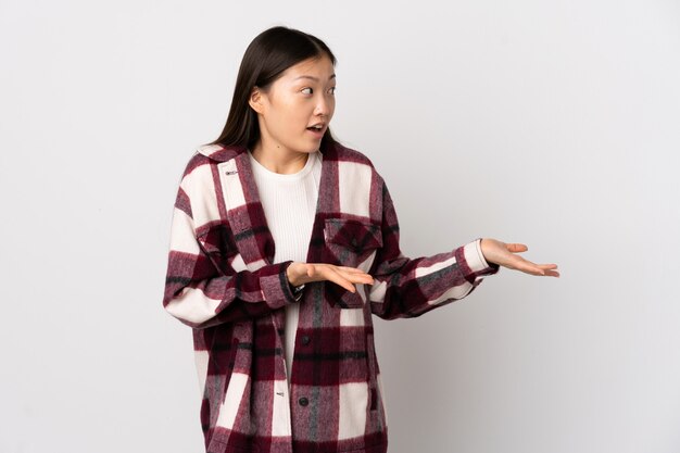 Молодая китайская девушка над изолированной белой стеной с выражением удивления пока смотрящ сторону