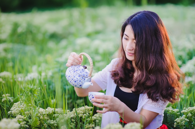 開花草原にお茶を注ぐ若い中国人の女の子