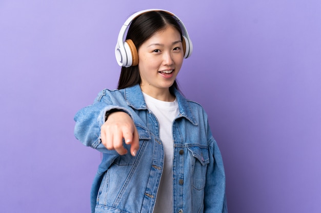 Young Chinese girl over purple wall listening music