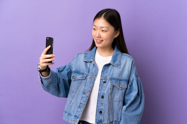 Молодая китайская девушка над фиолетовой стеной делая selfie