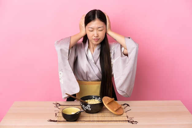 Young Chinese girl wearing kimono and eating noodles frustrated and coning ears