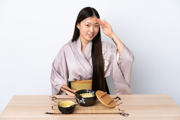 Giovane ragazza cinese che indossa il kimono e mangiare le tagliatelle salutando con la mano con l'espressione felice