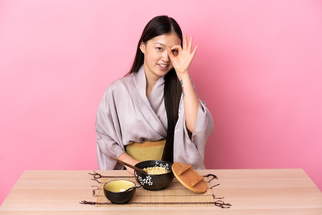 Young Chinese girl wearing kimono and eating noodles showing ok sign with fingers