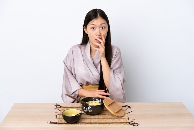 Молодая китаянка в кимоно и ест лапшу удивлена и шокирована, глядя вправо