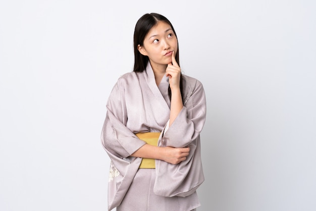 Young Chinese girl wearing kimono having doubts while looking up