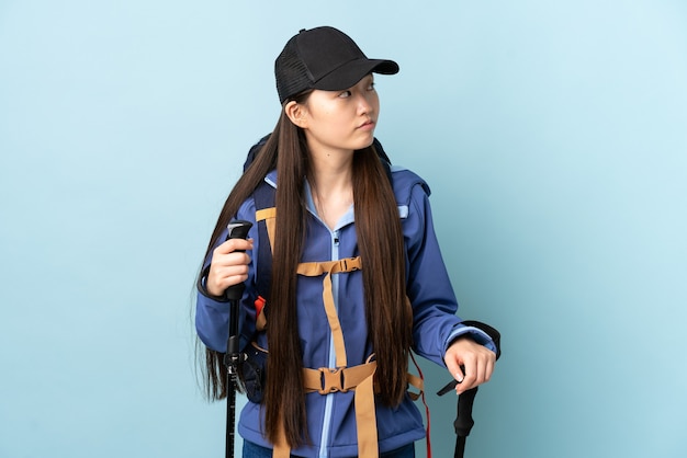 Giovane ragazza cinese con zaino e bastoncini da trekking su blu guardando al lato