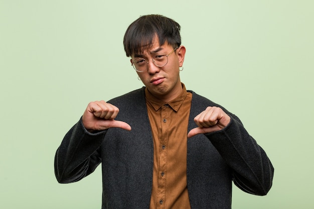 Young chinese man against a green wall