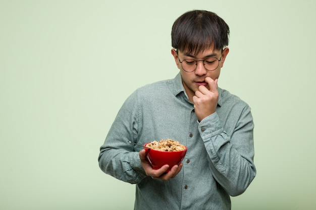 Молодой китайский человек ест миску каши