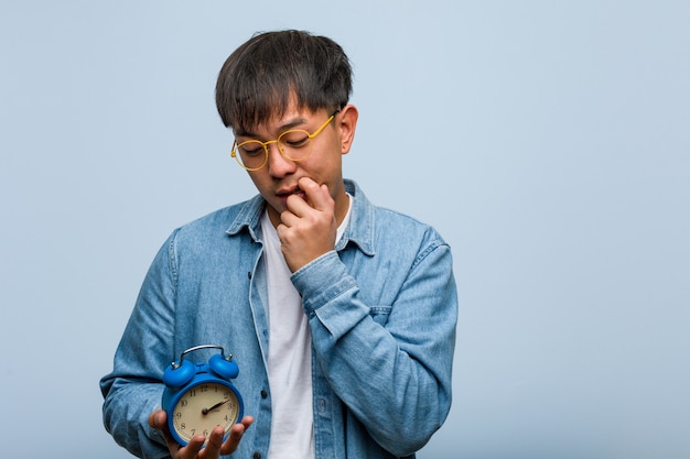 Young chinese man holding an alarm clock relaxed thinking about something looking at a copy space