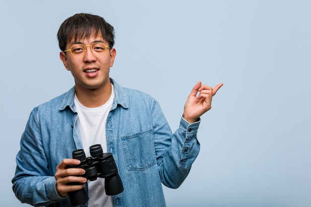 Young chinese man holding a binoculars pointing to the side with finger