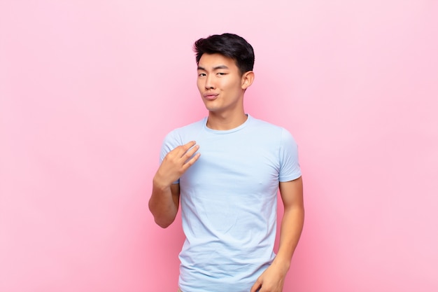 Young chinese man looking arrogant, successful, positive and proud, pointing to self against flat color wall