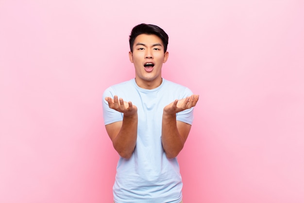 Young chinese man looking desperate and frustrated, stressed, unhappy and annoyed, shouting and screaming against flat color wall