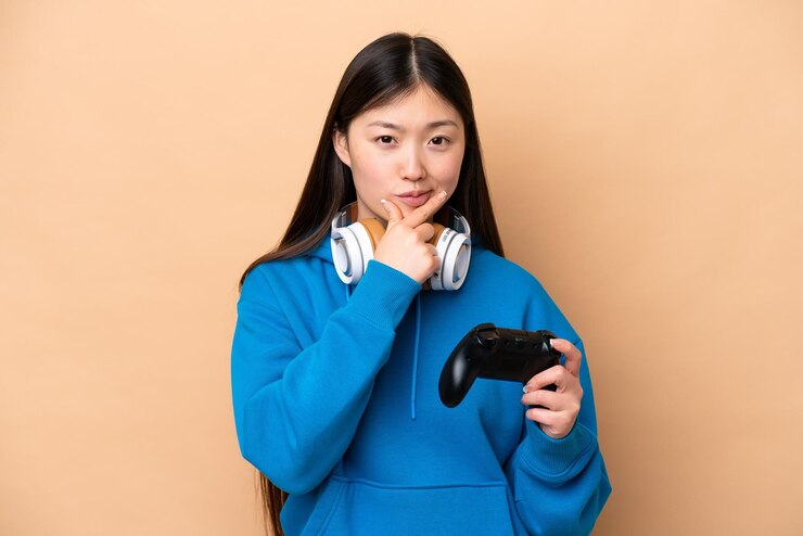 Photo ベージュの背景の思考に分離されたビデオ ゲーム コントローラーで遊ぶ若い中国人男性