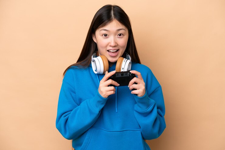 Photo 驚きの表情でベージュ色の背景に分離されたビデオ ゲーム コントローラーで遊ぶ若い中国人男性