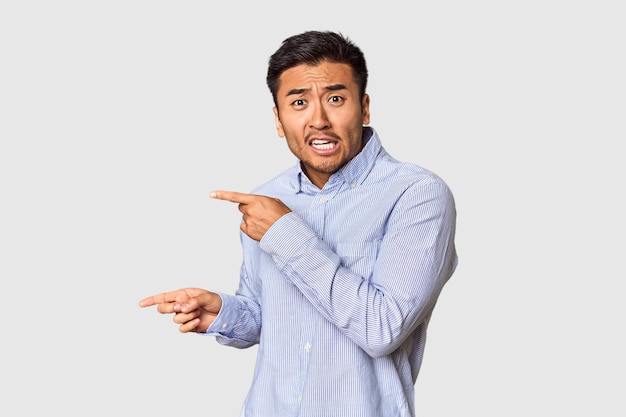 Young Chinese man in studio background shocked pointing with index fingers to a copy space