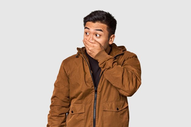 Photo young chinese man in studio background thoughtful looking to a copy space covering mouth with hand