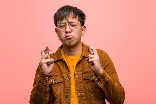 Young chinese man wearing a jacket crossing fingers for having luck