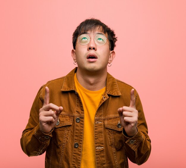 Young chinese man wearing a jacket surprised pointing up to show something