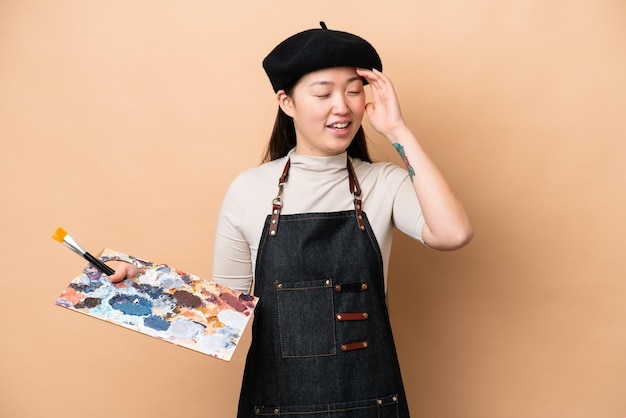 Young Chinese painter woman isolated on beige background smiling a lot