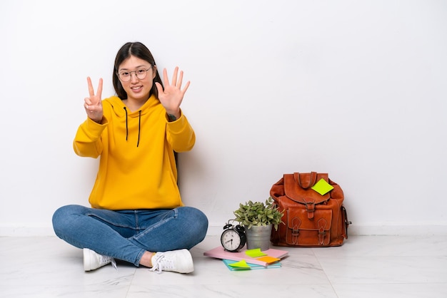 Young Chinese student woman sitting on the floor isolated on white wall counting seven with fingers