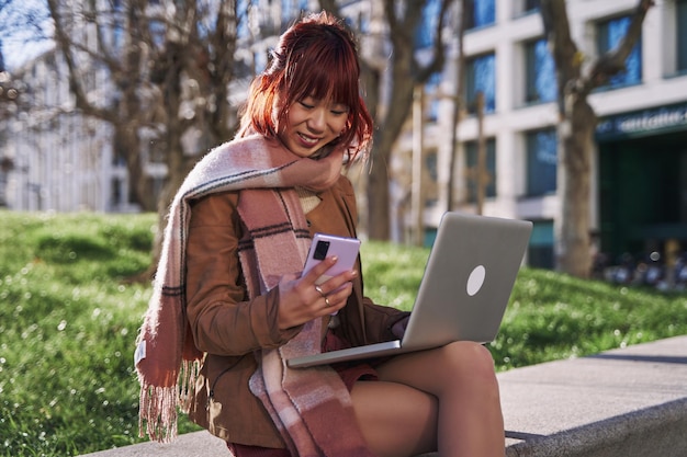 대학 캠퍼스에서 그녀의 휴대 전화를 사용하여 도시 여자에서 그녀의 노트북 컴퓨터를 사용하는 젊은 중국 십대