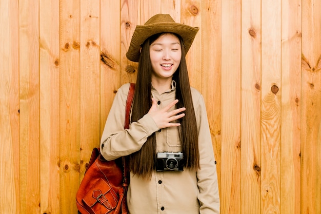 Young chinese traveler woman laughs out loudly keeping hand on chest.