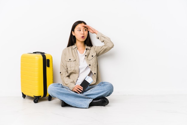 탑승권을 들고 앉아있는 젊은 중국 여행자 여자는 이마에 손을 잡고 멀리 찾고 있습니다.