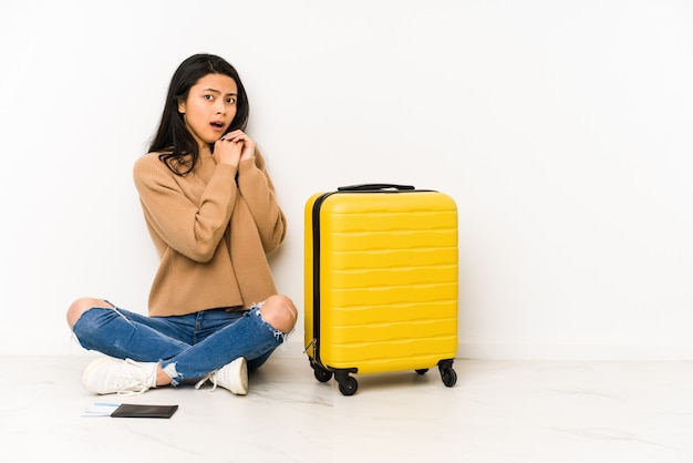 Young chinese traveler woman sittting on the floor with a suitcase isolated scared and afraid.