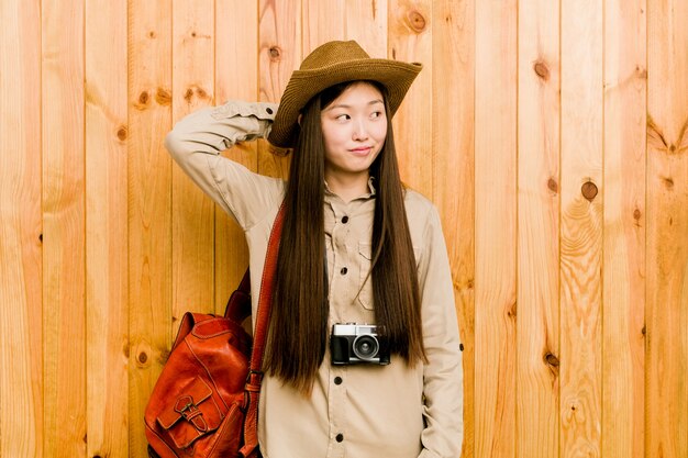 Young chinese traveler woman touching back of head, thinking and making a choice.