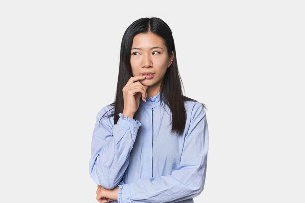 Photo young chinese woman in blue shirt relaxed thinking about something looking at a copy space