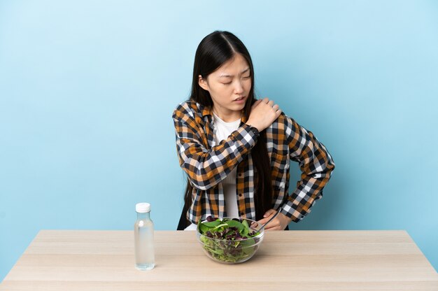 어깨에 통증이있는 샐러드를 먹는 젊은 중국 여성