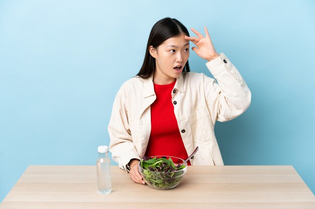 Young Chinese woman eating a salad with surprise expression while looking side