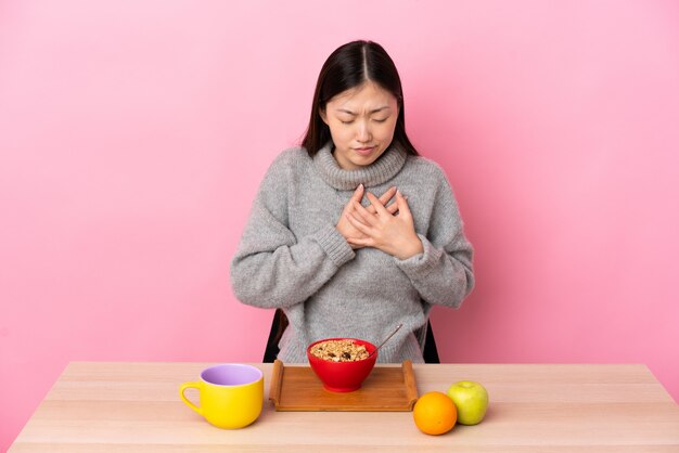 Young Chinese woman  having breakfast in a table having a pain in the heart